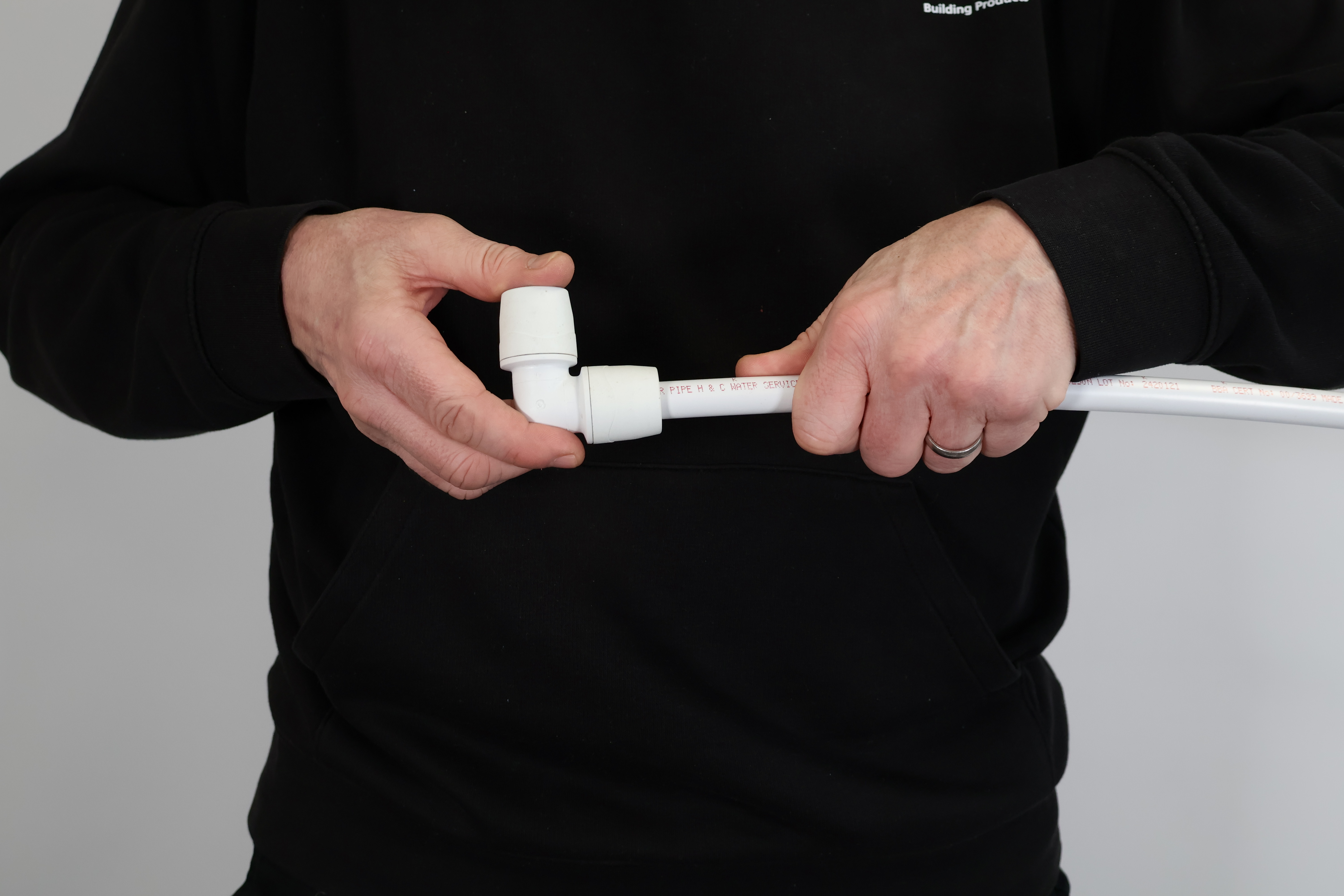 Close-up of a PolyMax push-fit elbow being checked for a secure fit. Proper hand-tightening ensures the pipe has passed through the grab ring and O-ring, preventing leaks and ensuring long-term joint integrity.