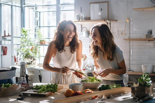 Two happy laughing women cooking together at white modern kitchen at home. Back light.jpg